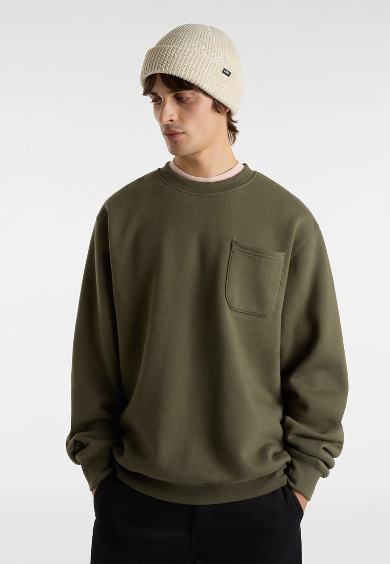 Olivengroene sweatshirt met een ronde hals, lange mouwen en een borstzak; gedragen met een lichtbeige geribde beanie.