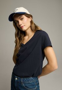 Granatowy top z krótkim rękawem o luźnym kroju, zestawiony z niebieskimi dżinsowymi szortami oraz białą czapką z granatowymi akcentami i detalem z logo.