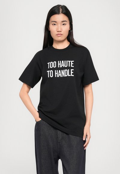 Melna kokvilnas T-kreklu ar brīvu piegriezumu, priekšpusē centrā balti burti "TOO HAUTE TO HANDLE". Īsās piedurknes un apaļš dekoltē.