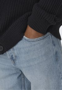 Námořnický ribbed cardigan s knoflíkovou detailní výzdobou, spárovaný se světle modrými džínami s opotřebením. Viditelná kapsa a roztrhaný lem.