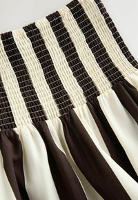 Jupe à taille smockée avec des rayures verticales alternées de brun foncé et de crème, présentant une texture fluide et plissée le long de l'ourlet.