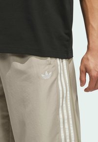 Crna majica s kratkim rukavima u kombinaciji s bež športskim kratkim hlačama koje imaju bijele tri pruge i bijeli izvezeni logo na lijevom bedru.