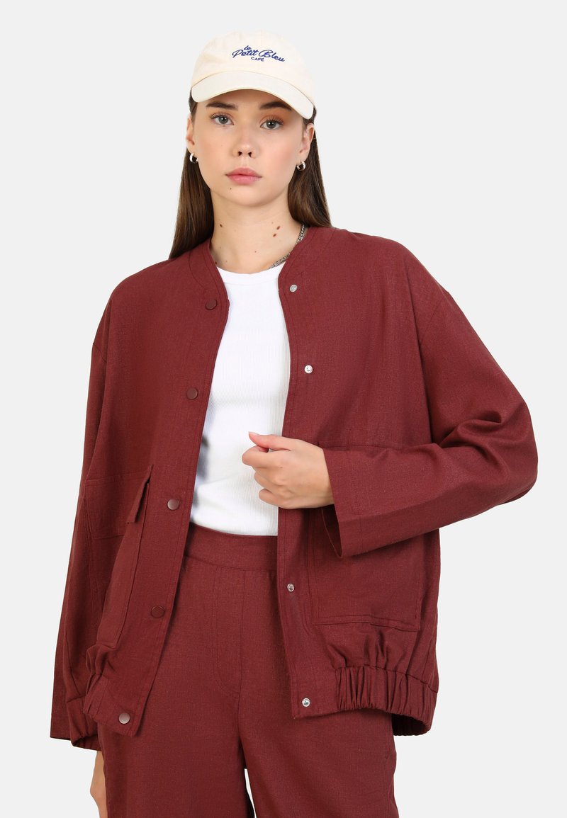 Bordeaux jack met een relaxed fit, voorzien van drukknoopsluitingen, zijzakken en gerimpelde manchetten. Draagt over een witte top en gecombineerd met bijpassende broek.
