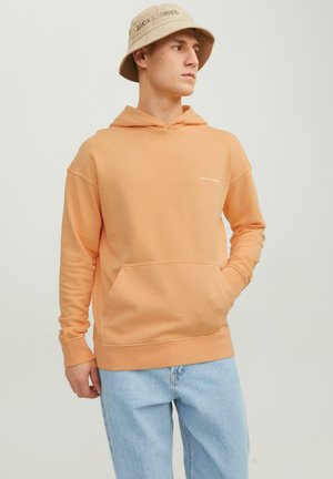 Helle orange Kapuzenjacke mit einer Kängurutasche, gerippten Bündchen und gesticktem Logo auf der Brust. Getragen mit hellblauen Jeans.
