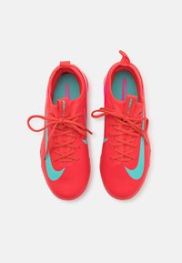 Červené tenisky Nike so štruktúrovaným zvrškom, tyrkysovým Swooshom a šnurovaním. Obsahujú polstrovaný interiér a kontrastnú modrú stielku.
