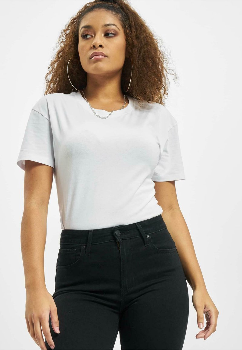 Hvit kortermet t-skjorte laget av myk bomullsvev, sammen med høyhalsede svarte jeans. Har et minimalistisk design og avslappet passform.