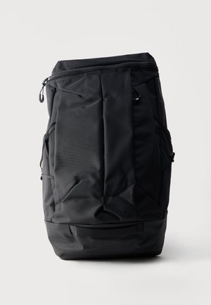 Sort lodret rygsæk med lynlås øverst, forlommel, sidelommer og en robust bund, stående mod hvid baggrund.