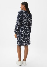 Robe bleu marine avec un motif abstrait blanc, manches longues, taille cintrée et une longueur aux genoux, associée à des baskets blanches.