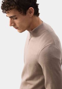 Beżowy sweter z wysokim kołnierzem i półzamkiem, charakteryzujący się gładką teksturą i dopasowanym krojem, podkreślający nowoczesny i elegancki styl.