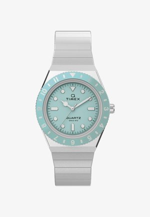 Timex kvarcni ručni sat sa srebrnim metalnim remenom, okruglim tirkiznim brojčanikom, bijelim oznakama sati i rotirajućim prstenom označenim brojevima od 1 do 12.