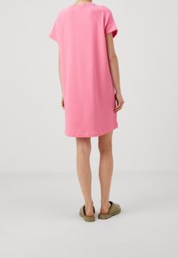 Vestido de camiseta rosa de gran tamaño con mangas cortas, fabricado en tela suave, que presenta un escote redondeado y un ajuste relajado, combinado con zapatos verdes tipo slip-on.