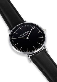 Reloj de pulsera analógico negro con acentos plateados. Presenta una caja redonda, una esfera negra con marcadores de horas minimalistas y una correa de cuero negra.
