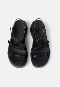 Černé kožené sandály s více popruhy, kulatými akcenty a texturovanou podrážkou. Obsahují nastavitelné zádové popruhy pro bezpečné uchycení.
