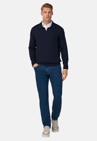 Tumši zila adīta pelēka ar platu apkakli, pārī ar zilām džinsu biksēm un gaisīgām sporta kurpēm. Gluda tekstūra un brīvs piegriezums.