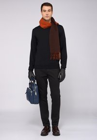 Černý svetr, hnědý šátek s třásněmi, tmavé kalhoty, kožené rukavice a tmavě hnědé boty; modrá taška se stříbrnými doplňky.