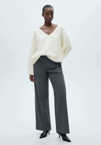 Cremfarbener V-Ausschnitt-Pullover mit lockerer Passform und geribbelter Textur, kombiniert mit schiefergrauen, gestreiften, weiten Hosen und spitzen schwarzen Heels.