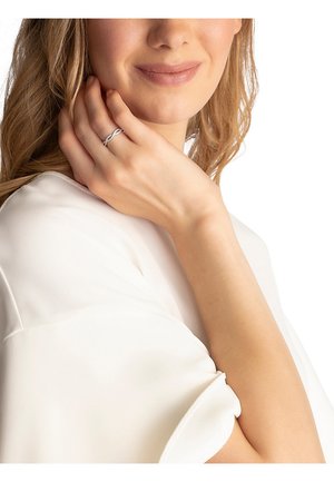 Zilveren ring met een gedraaide ontwerp, gladde textuur en glanzende afwerking, gedragen aan een hand met lichte huid, tegen een witte blouse.