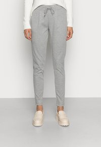 Grå, slim-fit joggebukser med snøring i livet, med lommer foran og en myk tekstur. Bært med lyse, slip-on sko.