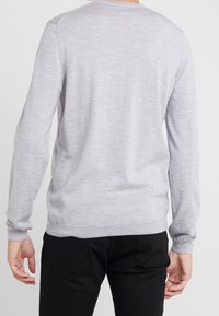 Pull gris en tricot avec encolure ronde, manches longues et texture lisse, associé à un pantalon noir. Design simple sans motifs visibles.