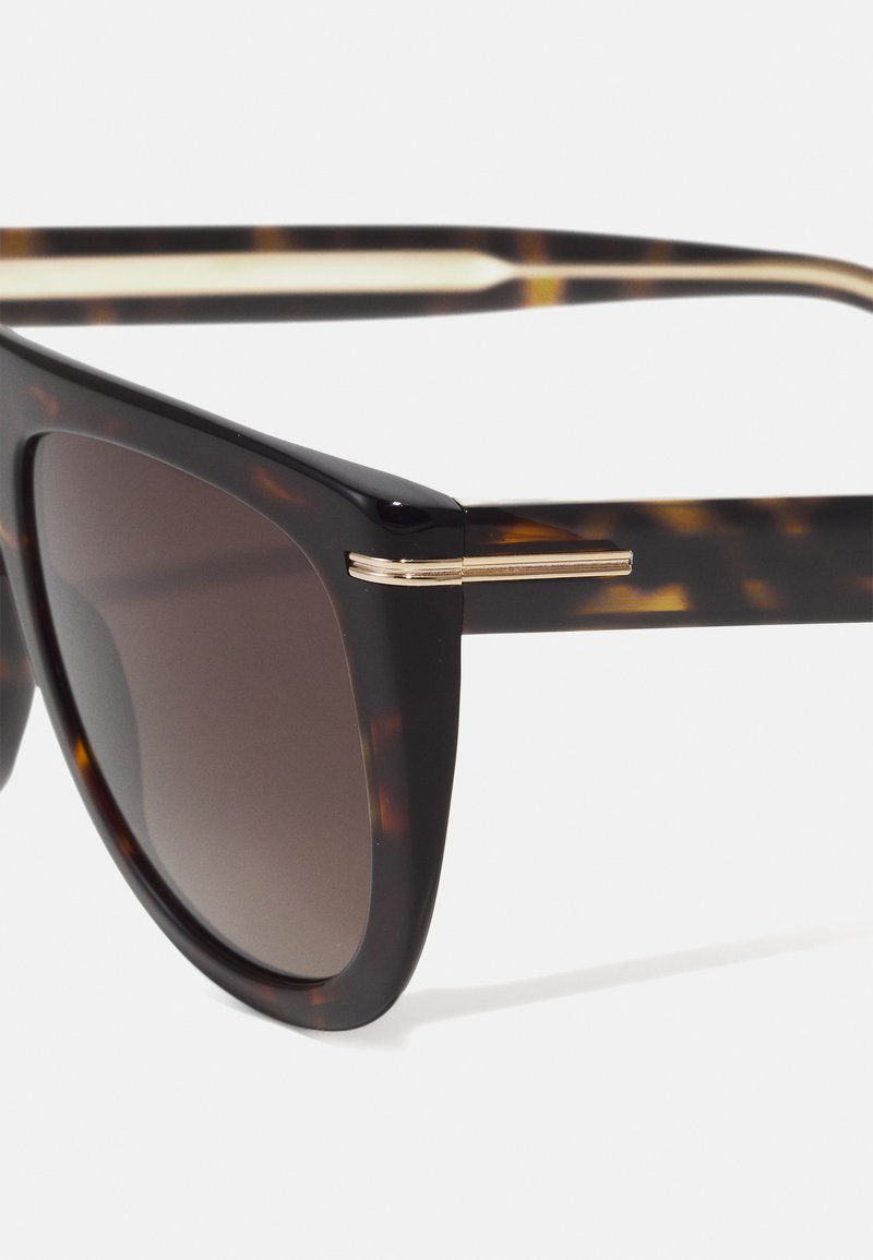 Sonnenbrille aus Schildpatt mit dunklen Gläsern, die einen eleganten schwarzen Rahmen und goldfarbene Metallakzente an den Bügeln bietet. Glänzende Oberflächenbeschichtung.