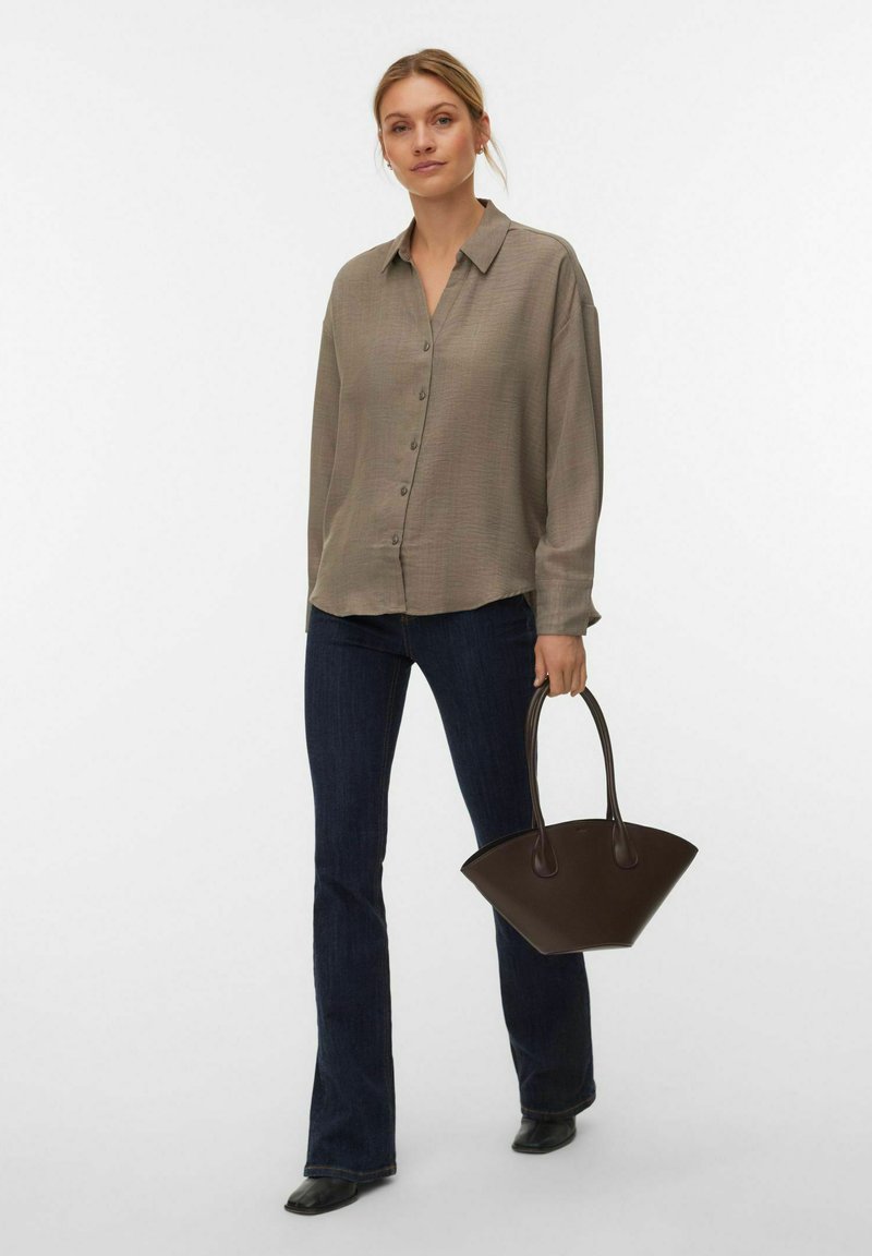 Chemise boutonnée, de couleur brun clair, avec un col et une coupe décontractée, associée à un jean évasé foncé et un sac à main brun incurvé. Texture lisse.