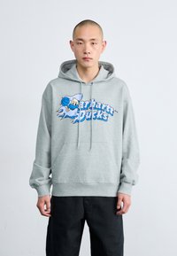 Haut à capuche gris avec poche kangourou et cordon de serrage réglable, présentant une impression graphique bleue d'un personnage et le texte "Bucks." Texture caoutchouteuse.