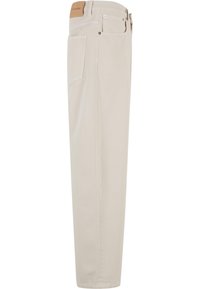 Pantalon beige décontracté à coupe droite avec poches avant et arrière, passants pour ceinture et écusson en cuir beige sur la taille.