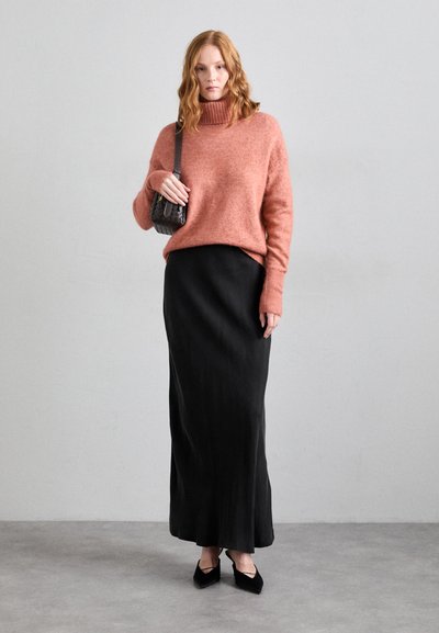 Rust-colored, chunky knit sweater with a high collar, paired with a long black skirt. Black pointed-toe heels and a small textured bag.