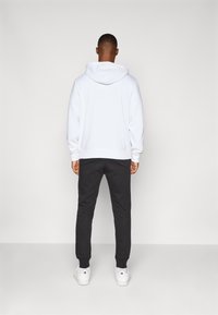 Witte hoodie met een trekkoordcapuchon, gecombineerd met zwarte joggingbroek en witte sneakers. Zachte textuur; casual sportieve stijl.