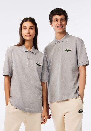 Polos grises de mezcla de algodón, con mangas cortas, dos botones y un logo bordado verde en el pecho. Combínalos con pantalones beiges.