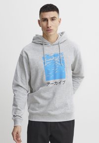 Grå hættetrøje med snørebånd, prydet med et blåt grafisk design af vand og japansk tekst nedenfor. Blød tekstur, afslappet pasform.