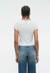 Λευκό κοντομάνικο εφαρμοστό μπλουζάκι συνδυασμένο με τζιν παντελόνι μπλε, ψηλόμεσο, με απαλό ντεγκραντέ φινίρισμα και δύο πίσω τσέπες.