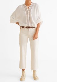 Løs hvid bluse med blonde detaljer, stylet med cremefarvede, cropped jeans og beige høj-til-an-kot-sneakers. Enkelt design og neutrale nuancer.