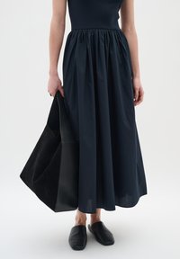 Tengerészkék, rakott derekú, bővülő szoknya, fekete velúr táskával és fekete slip-on cipőkkel párosítva. Sima anyag textúra.