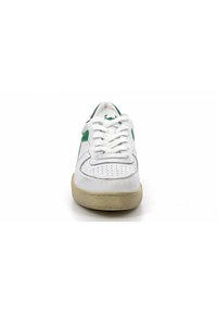 Sneaker in pelle bianca con accenti verdi, lacci piatti e punta perforata. Suola in gomma color crema con lievi segni di usura. Design minimalista.