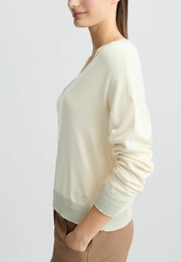 Maglione v-neck color crema chiaro realizzato in tessuto morbido con orlo e polsini a costine, caratterizzato da un discreto dettaglio del logo vicino alla vita.