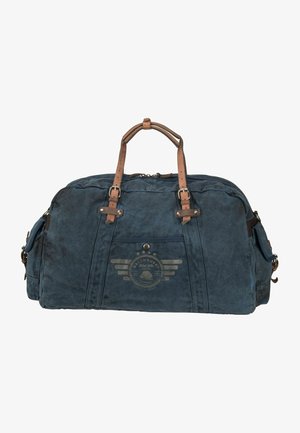 Blauwe canvas duffeltas met bruine lederen accenten, met een logo ontwerp aan de voorkant, twee handvatten en ritssluitingen aan de zijkanten.