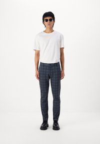 Camiseta blanca de manga corta combinada con pantalones a cuadros azules. El modelo lleva gafas de sol negras y zapatos oscuros. Diseño simple y discreto.