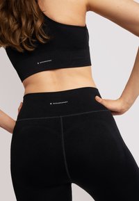 Reggiseno sportivo nero a costine e leggings a vestibilità aderente. Presenta dettagli del logo visibili e cuciture a contrasto. Texture morbida.