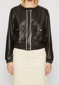 Sort faux læder cropped jakke med hvid lynlås, to forlommer, elastisk talje og manchetter, samt diskret branding på brystet.