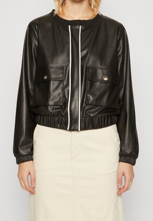 Zwarte neplederen cropped jack met witte rits, twee voorkruiszakken, elastische tailleband en manchetten, en subtiele branding op de borst.