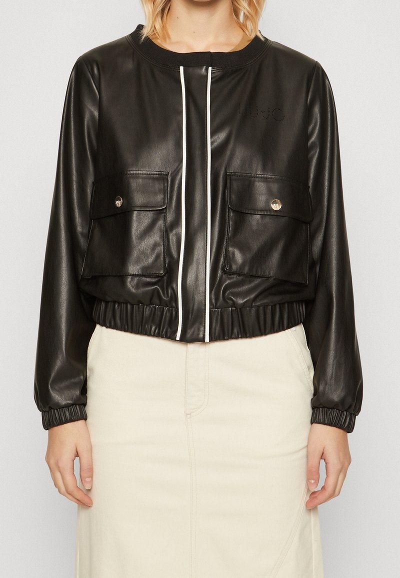 Sort faux læder cropped jakke med hvid lynlås, to forlommer, elastisk talje og manchetter, samt diskret branding på brystet.