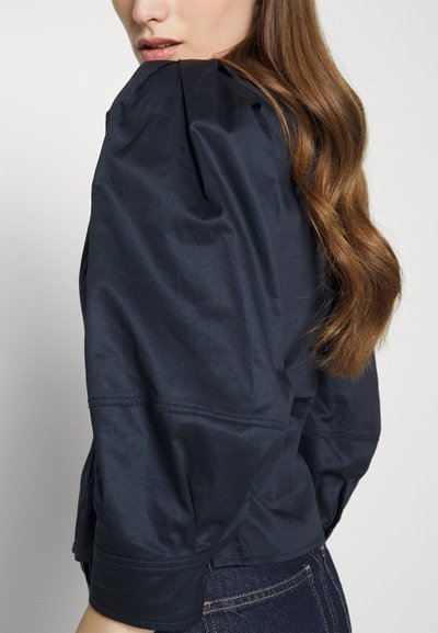 Ναυτικό μπλε τζάκετ με φουσκωτά μανίκια, απαλό υλικό, δομημένους ώμους και ραμμένες λεπτομέρειες. Συνδυάζεται με σκούρο τζην παντελόνι.