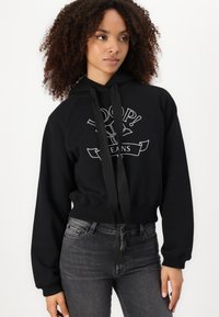 Black cropped hoodie made from cotton blend, featuring a graphic print, kangaroo pocket, and drawstring hood. Paired with dark gray jeans.