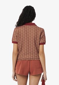 Korte mouw polo in het rood met een gestructureerd geometrisch patroon, voorzien van een geribde kraag en bijpassende korte broek in een effen roestkleur.