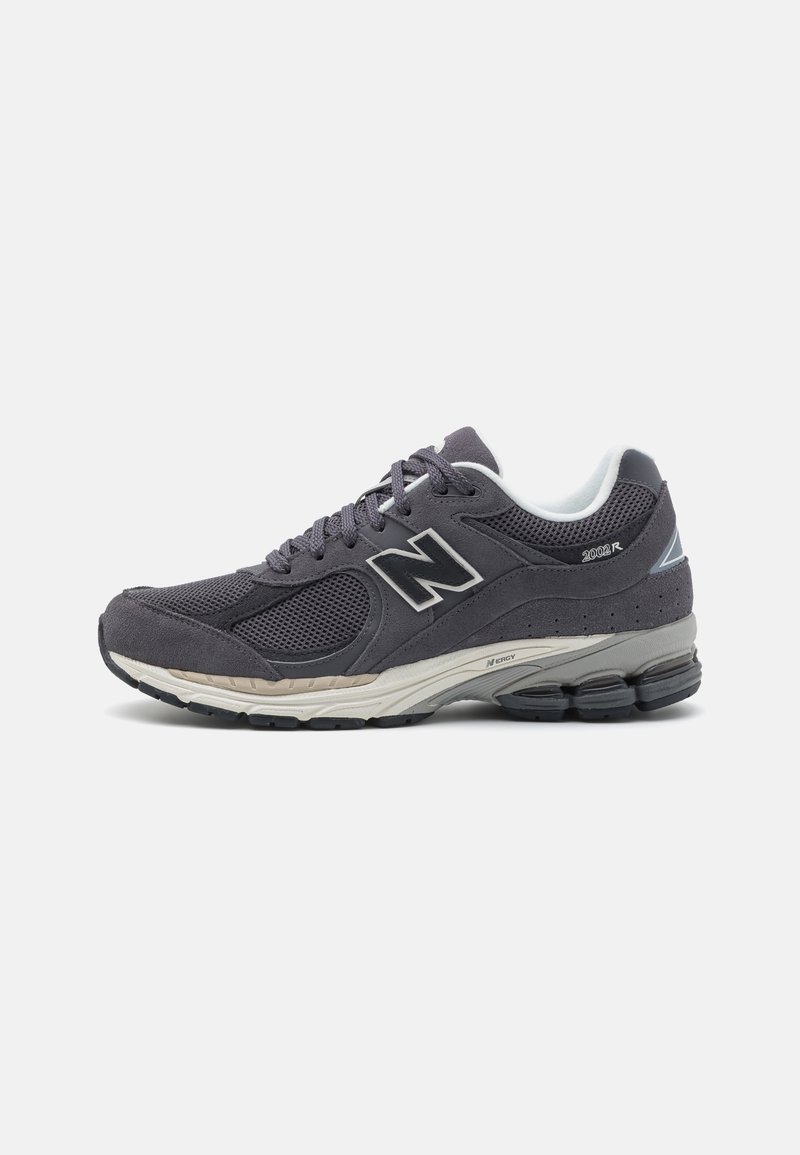 Baskets de sport gris foncé avec panneaux en mesh et en daim, semelle blanche coussinée, semelle noire et lacets, présentées de profil sur fond blanc.