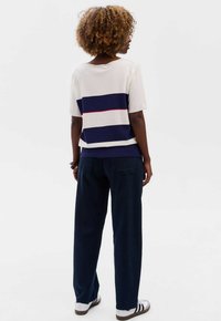 Korte mouw gebreide top met horizontale strepen in marineblauw, wit en rood. Gecombineerd met donkerblauwe losse broek en witte sneakers.