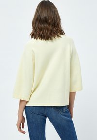 Maglione oversize giallo chiaro in tessuto texturizzato, con maniche a tre quarti e orlo dritto. Abbinato a jeans in denim.