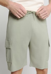 Lichtgroene cargoshorts met een elastische tailleband, een trekkoordsluiting en twee zijzakken. Glad materiaal met een relaxte pasvorm.