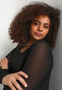 Black polka-dot long-sleeve top with a round neckline, featuring a sheer texture and fitted design, worn by a person with curly hair.
